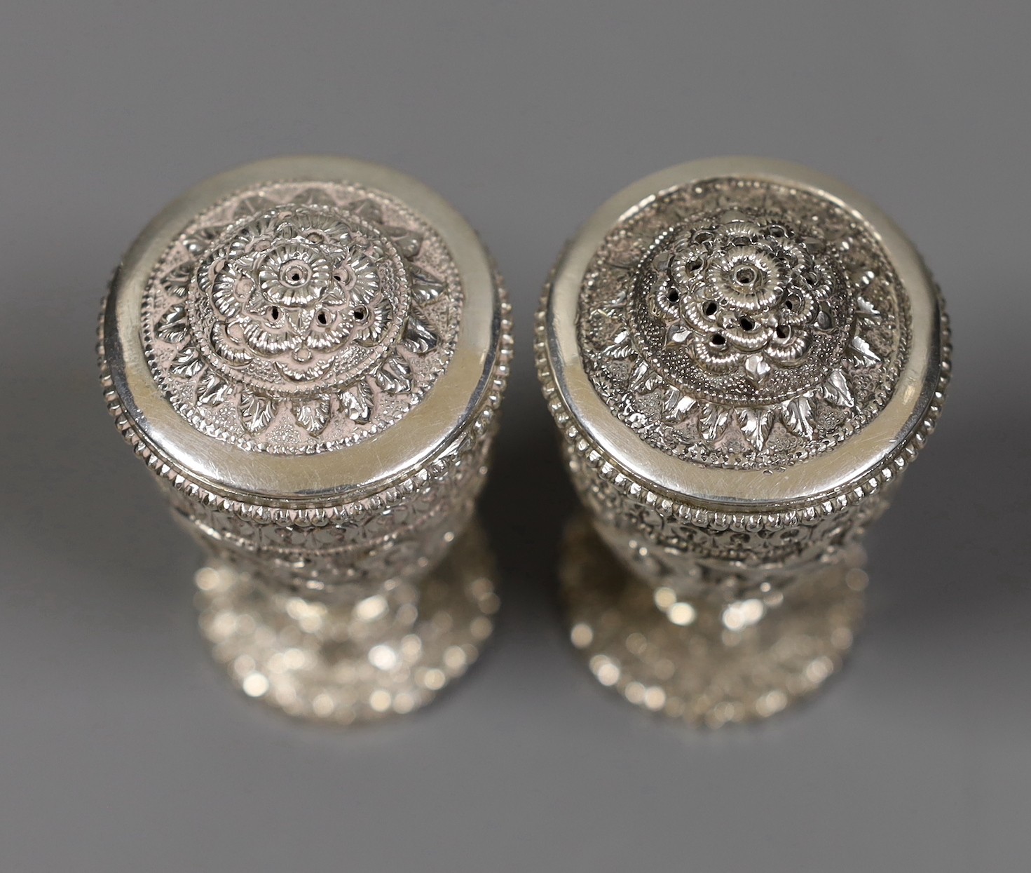 A pair of early 20th century Indian embossed white metal pedestal pepperettes, 7cm, 112 grams, in Elkington & Co, Calcutta, fitted box.